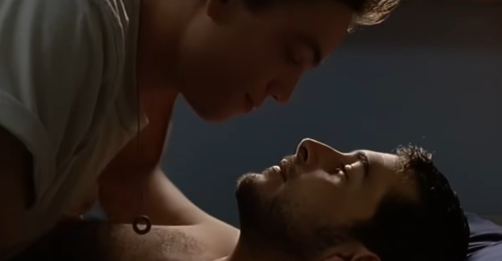 Deux hommes dans une scène intime et romantique allongés sur un lit dans une ambiance tamisée