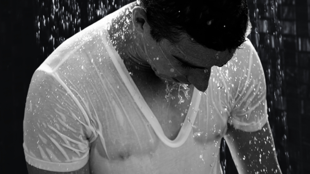 Homme sous la pluie portant un t-shirt blanc mouillé, illustrant les doutes émotionnels après une rencontre sexuelle éphémère.